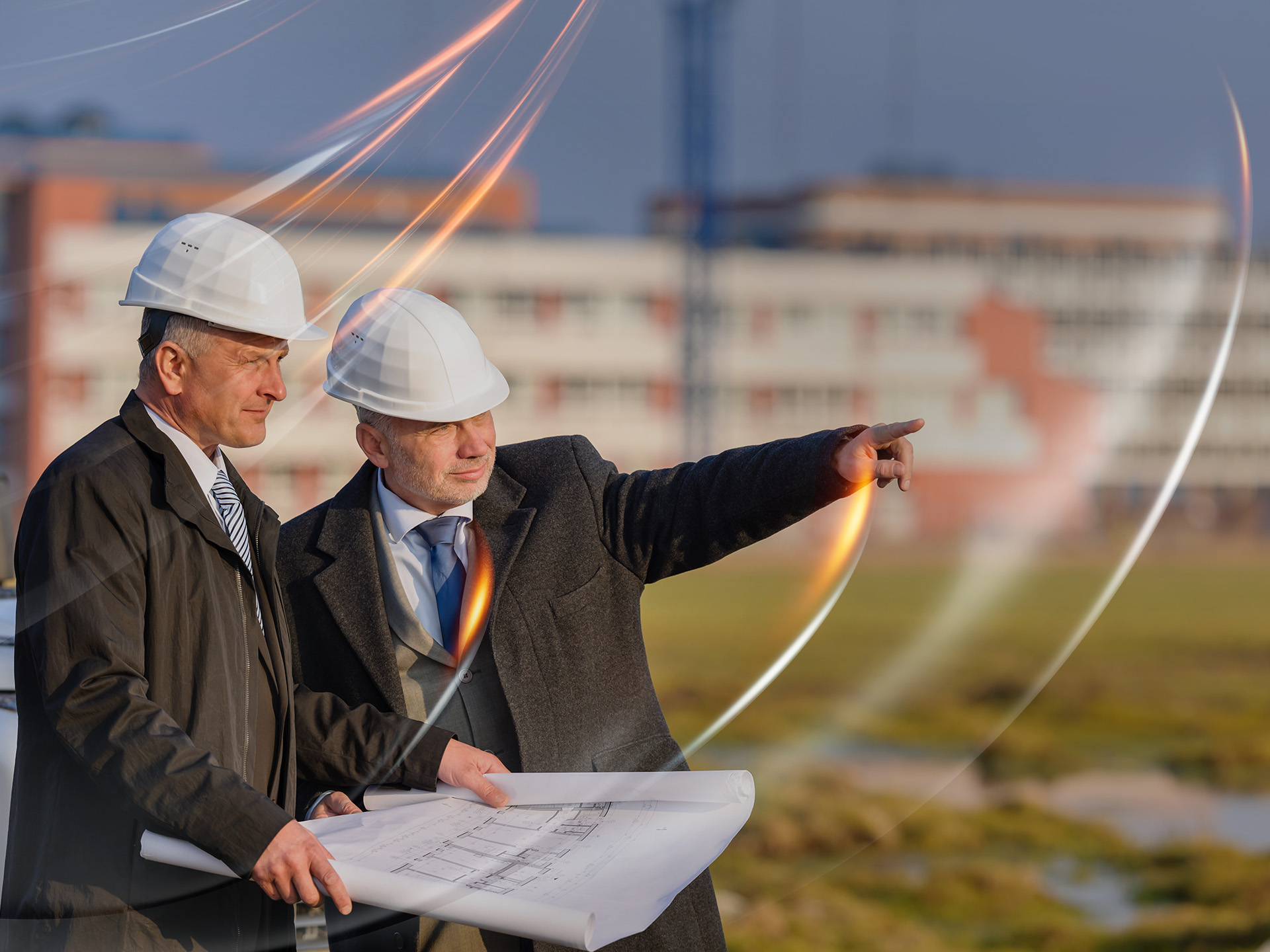 Two men in smart suits and hard hats holding construction plans.