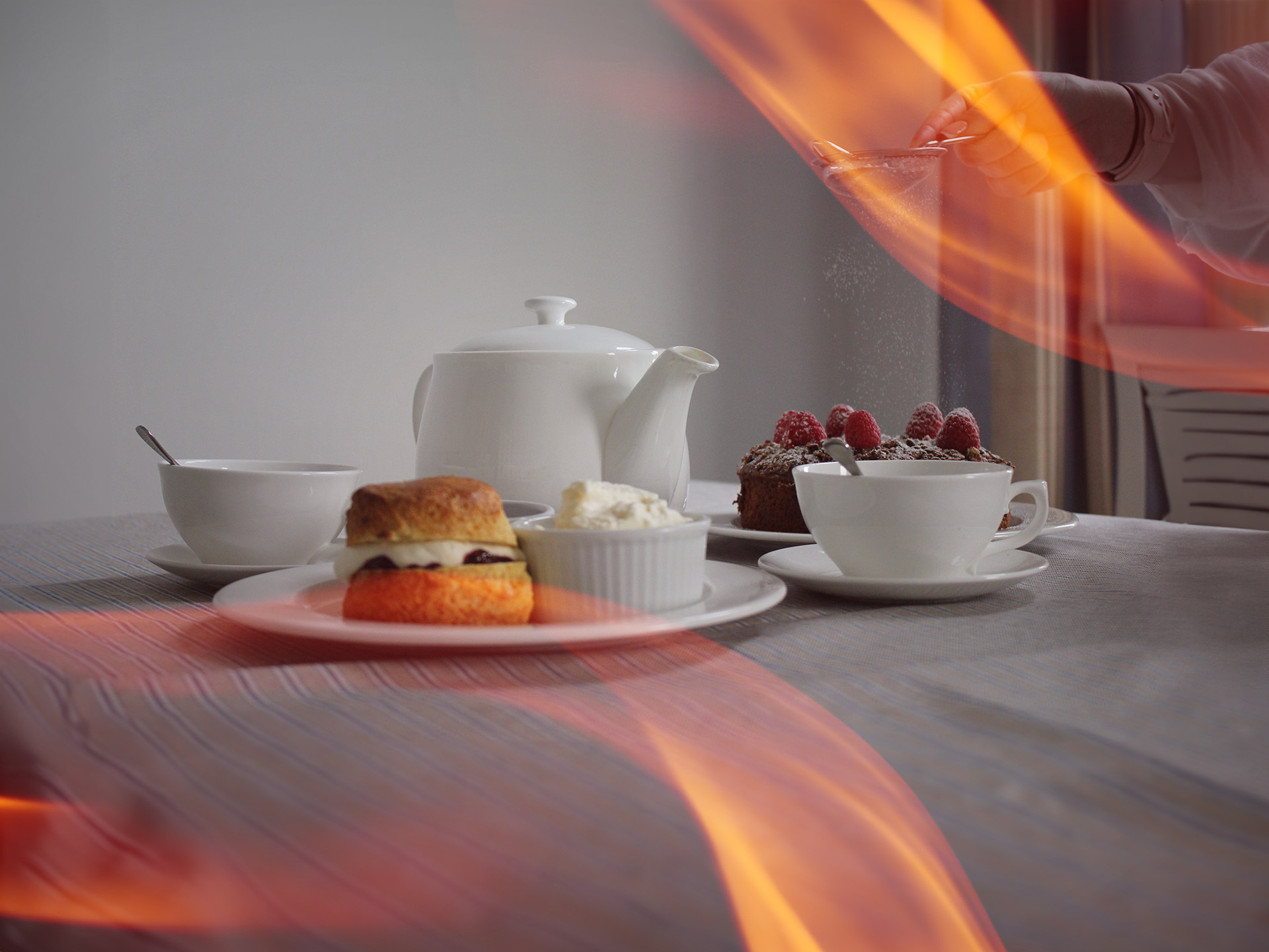 White tea set with a scone and cream, and a chocolate cake getting icing sugar dusted over the top of it.