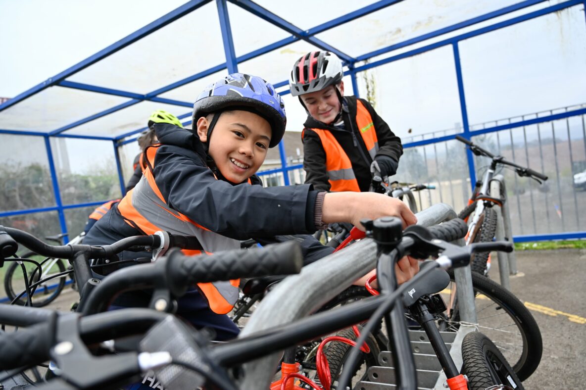 Two young boys wearing helmets and high visibility vests taking their bikes out of bike locks.